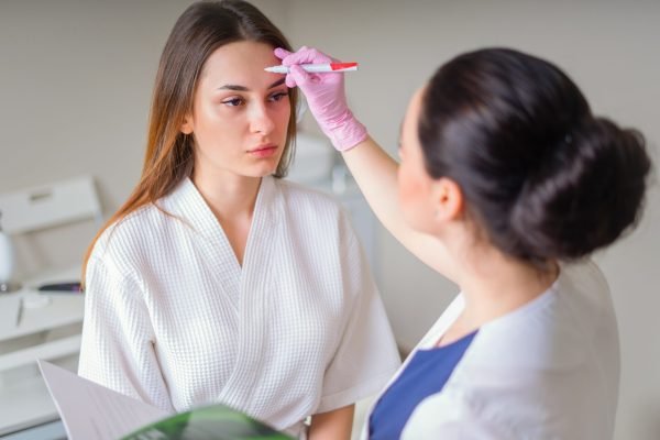 Cosmetologist ready to paint lines with marker on face of a patient