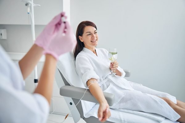 lovely-dark-haired-female-patient-with-glass-drink-her-hands-undergoing-intravenous-vitamin-therapy