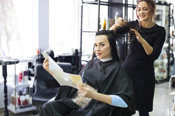 Professional hairdresser preparing to give a haircut to her beautiful cheerful female client combing her hair. Beauty industry service
